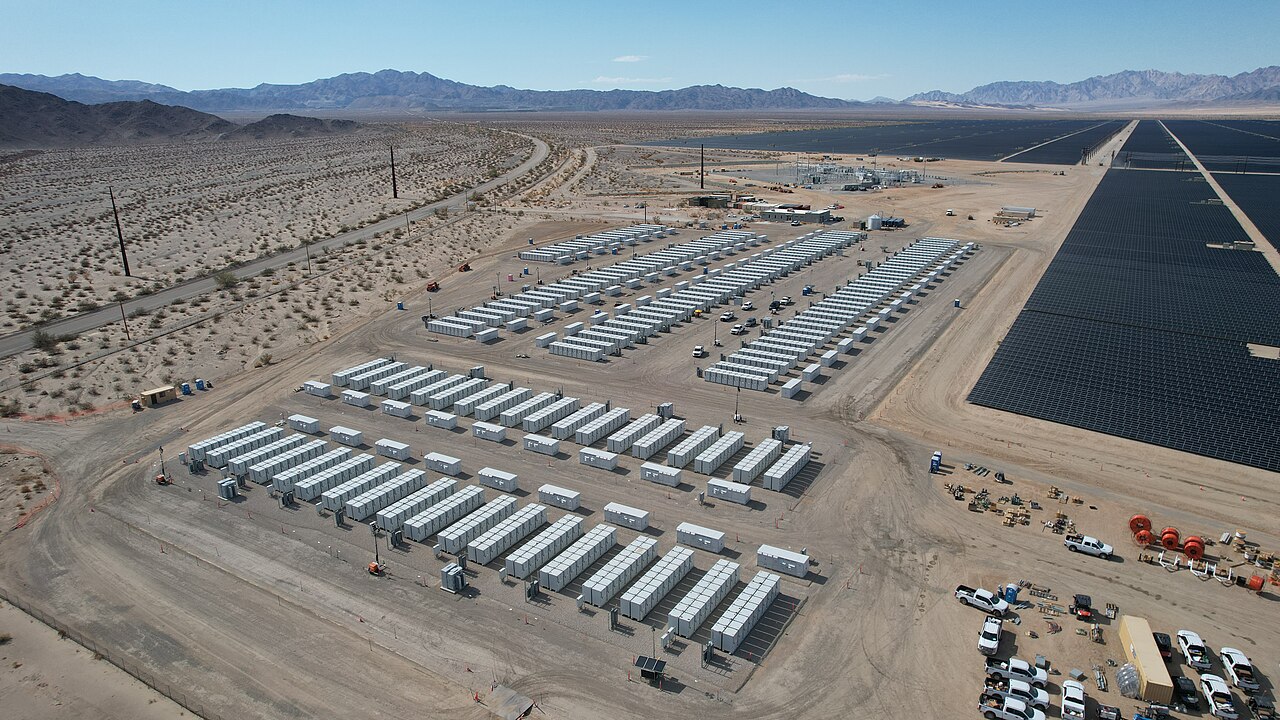 Aerial view of a utility-scale battery energy storage installation with rows of containers next to a solar field.